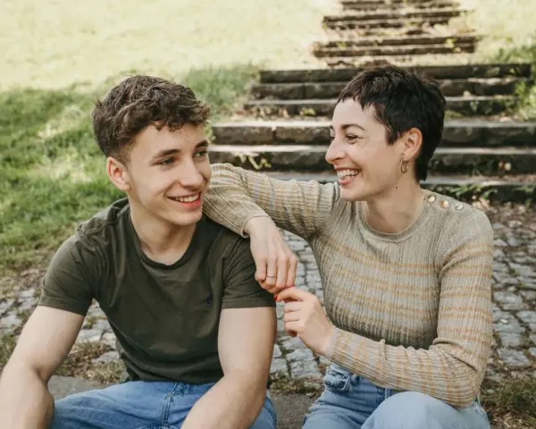 Ein lachendes Mutter-Sohn-Gespann sitzt im Freien vor einer Steintreppe.