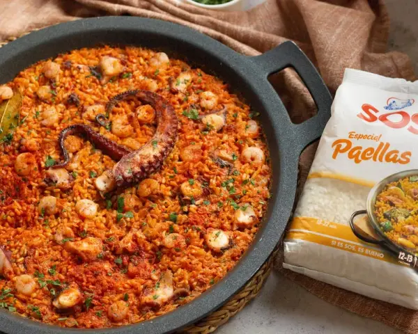 Paella de marisco con un tentáculo de pulpo visible, gambas y trozos de calamar. Al lado, un paquete de arroz SOS Especial Paellas.