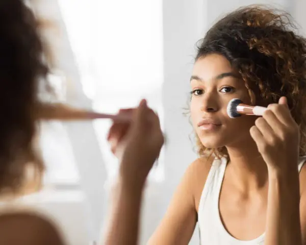 Une jeune femme applique du fond de teint avec un pinceau. Elle se demande combien de temps garder une palette de maquillage pour une peau parfaite.