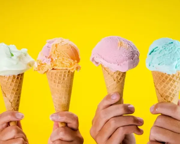 Vier Hände halten bunte Speiseeiswaffeln vor gelbem Hintergrund. Die ideale Temperatur für Speiseeis.