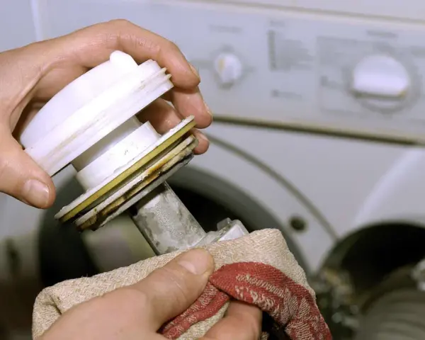 Hände reinigen das Flusensieb einer Bosch Waschmaschine. Regelmäßige Pflege sorgt für einwandfreie Funktion.