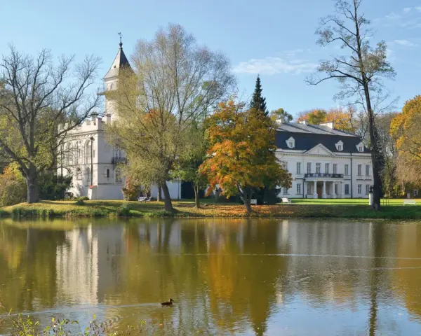 Pałac w jesiennej scenerii nad jeziorem, część Bolimowskiego Parku Krajobrazowego. Kaczka pływa po wodzie.