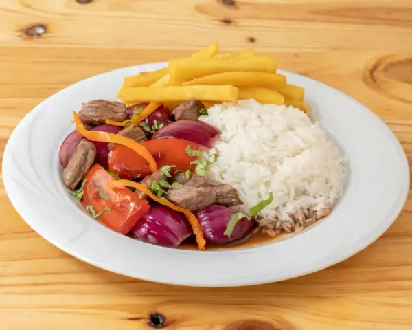 Lomo saltado con arroz blanco, papas fritas, carne, cebolla roja y tomate. Un plato peruano delicioso.