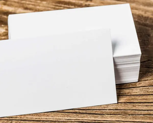 Pila de tarjetas de visita blancas sobre madera. Se aprecian los diferentes grosores de papel en la pila.