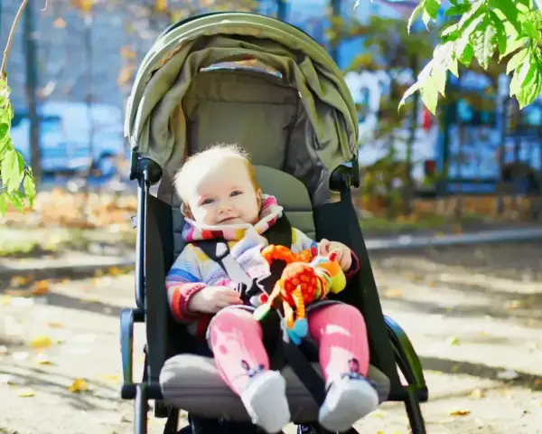 Uśmiechnięte dziecko w wózku spacerowym, z kolorową zabawką. Czas na spacer, do kiedy gondola posłuży?