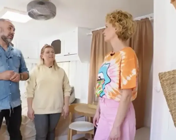 Trzy osoby omawiają remont przyczepy kempingowej. Wnętrze jest jasne, z widocznym łóżkiem i meblami.