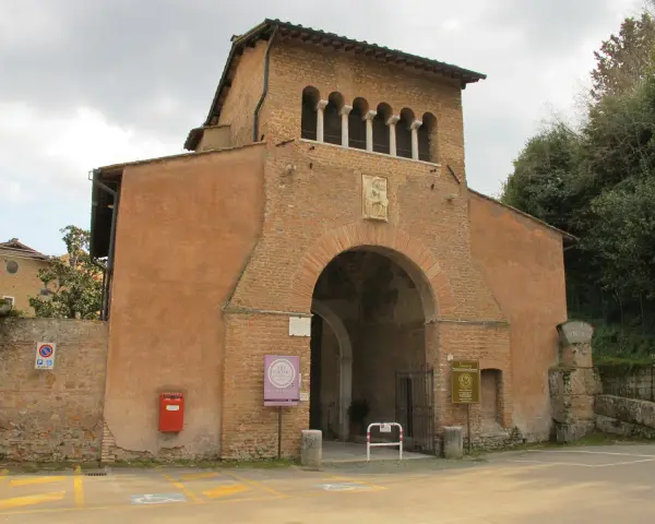 The imposing facade of Tre Fontane Abbey, with its arched entrance and upper loggia, stands against a cloudy sky.