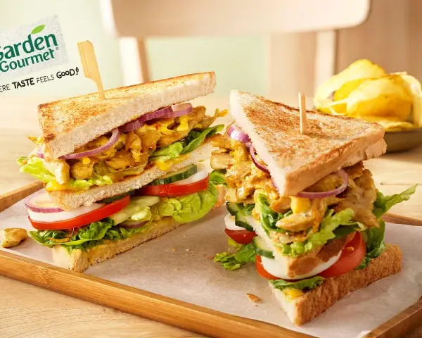 Zwei üppige Garden Gourmet Club Sandwiches mit knackigem Salat, Tomaten, Gurken und Zwiebeln auf getoastetem Brot.