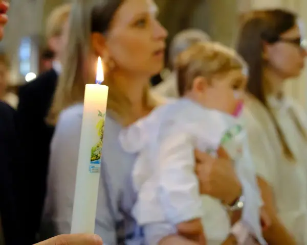 Chrzest dziecka. Czy świadek chrztu musi mieć zaświadczenie? Płonąca świeca chrzcielna w dłoniach.