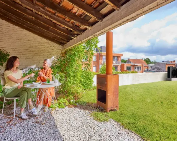 Due donne brindano su un terrazzo con prato. Sullo sfondo, una pompa di calore sul tetto.