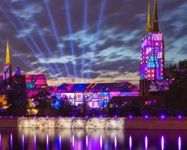 Ostrów Tumski we Wrocławiu nocą, rozświetlony kolorowymi projekcjami i niebieskimi snopami światła.