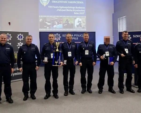 Policjanci w mundurach stoją w rzędzie, niektórzy trzymają nagrody i dyplomy.
