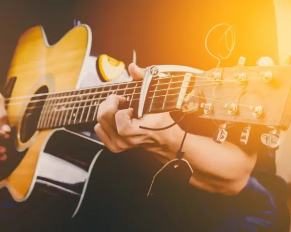 Osoba gra na gitarze akustycznej. Zastanawiasz się, ile trwa nauka gry na gitarze? To zależy od Ciebie!