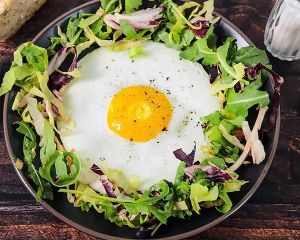 Un uovo occhio di bue su un letto di insalata mista, servito con pane integrale e condimenti.