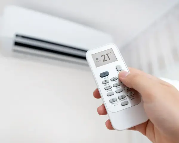 Mano ajustando el aire acondicionado a 21°C en modo "Cooling". La pantalla del control remoto muestra la temperatura y el modo, indicando que significa "cool" en el aire acondicionado: enfriar.