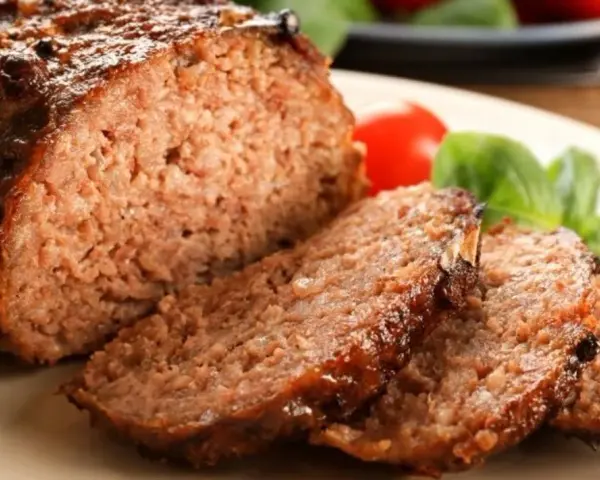 Soczysta, rumiana pieczeń rzymska, pokrojona w plastry, z pomidorkami i bazylią. To najlepsza pieczeń rzymska, jaką można sobie wymarzyć!