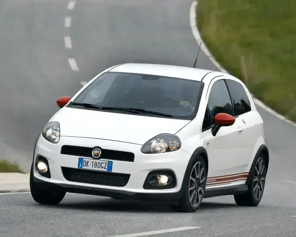 Biały Fiat Punto Evo Abarth z czerwonymi lusterkami pędzi po zakręcie drogi.