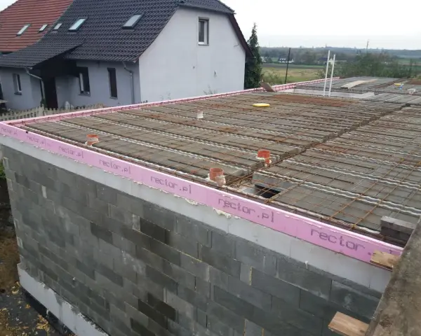 Budowa stropu zbrojonego, widoczne pustaki, różowa izolacja z napisem rector.pl i siatka zbrojeniowa.