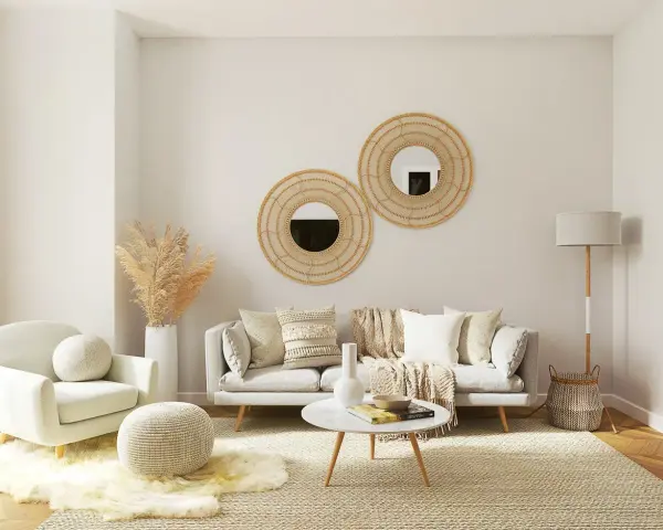 Salotto accogliente con divano grigio, poltrona bianca, tavolino rotondo e specchi decorativi in rattan. Un esempio di come arredare case moderne con stile boho-chic.