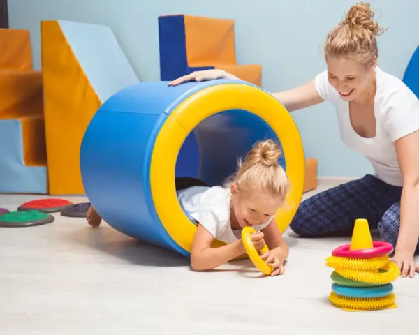 Dla kogo wczesne wspomaganie rozwoju? Dla małej dziewczynki bawiącej się w tunelu z terapeutką.