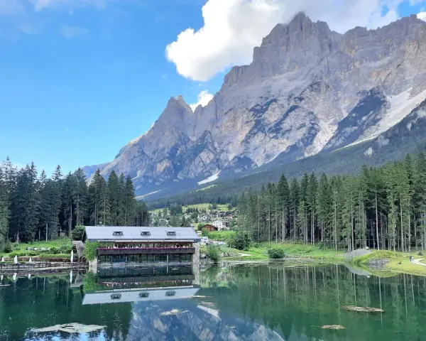 Riflessi alpini sul lago di Mosigo, con un rifugio e montagne imponenti sullo sfondo.