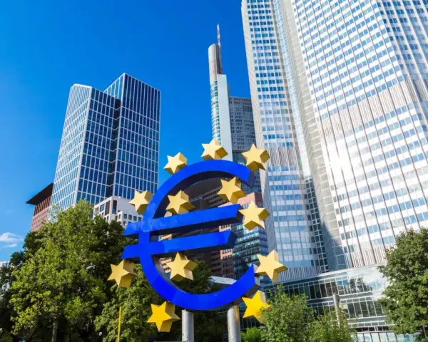 Symbol euro przed nowoczesnymi wieżowcami, siedziba europejskiego banku centralnego.