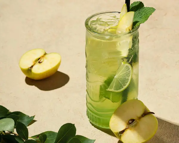 En uppfriskande p2 drink med äpple, lime och mynta. Två halvor av ett grönt äpple ligger bredvid glaset.