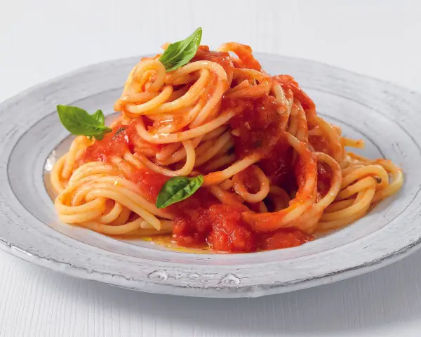 Un piatto di pasta fatta in casa, spaghetti al pomodoro fresco e basilico, serviti su un piatto rustico.