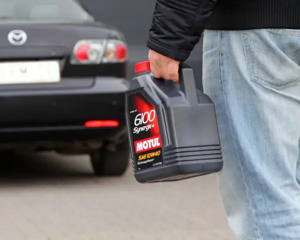 Mężczyzna niesie kanister z olejem silnikowym Motul. W tle czarna Mazda.