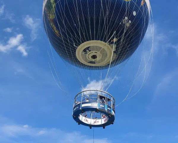 Weltballon über Berlin bei schönem Wetter. Die Gondel mit Passagieren schwebt unter dem riesigen Globus-Ballon.
