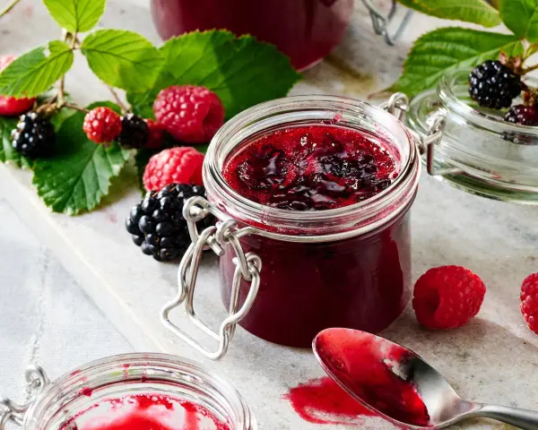 Frische Brombeeren und Himbeeren neben einem Glas selbstgemachter Marmelade. Perfekt für brombeeren rezepte schnell und einfach.
