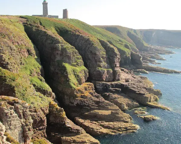 Scogliere verdi e rocciose con un faro in cima. Ideale per consigli su **Bretagna in moto**.