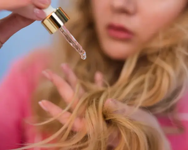 Kropla olejku do włosów rozjaśnianych spada na dłoń, która delikatnie przeczesuje blond kosmyki.
