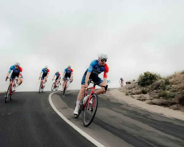 Cyclists in blue and red kits race downhill, showcasing the intense effort behind the Tour de France average speed.