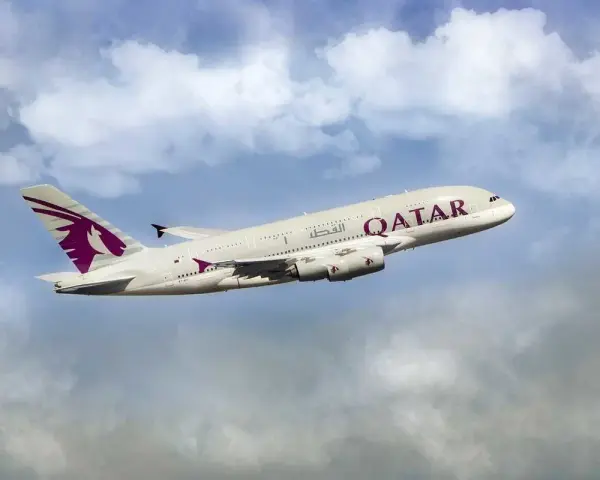 Qatar Airways Airbus A380 airplane in flight against a cloudy blue sky.