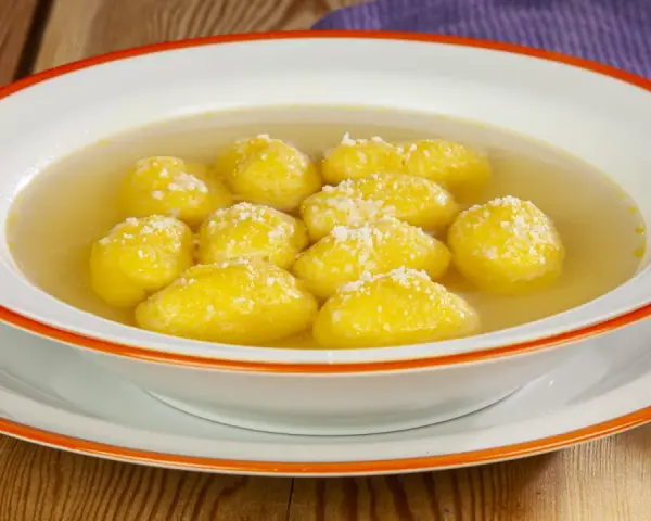 Una ciotola di semolino dosi per 1 persona, con palline dorate in brodo, cosparse di formaggio grattugiato.