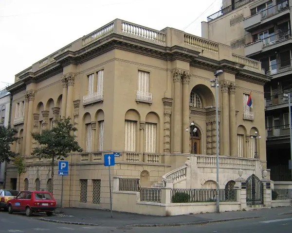 Elegancki budynek, Muzeum Tesli, z kolumnami i łukami. Przed nim schody i ogrodzenie.