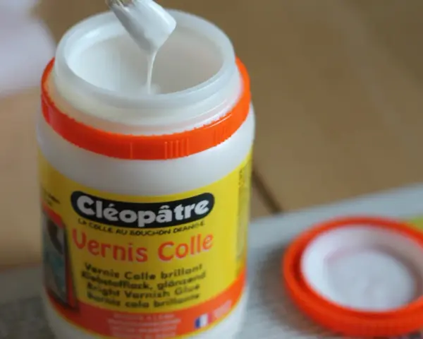 Un pinceau trempe dans un pot de vernis colle Cléopâtre, prêt à protéger une peinture acrylique.