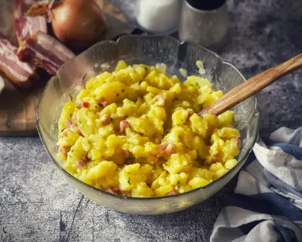 Ein Schüssel voller warmer Kartoffelsalat mit Speck und Zwiebeln, bereit zum Servieren.
