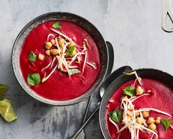 Zwei Schalen cremiger, **roter Bete Suppe mit Kokosmilch und Orangensaft**, garniert mit Kichererbsen und Sprossen.
