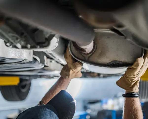 Mani guantate lavorano sul sistema di scarico di un'auto, forse sostituendo il catalizzatore auto.