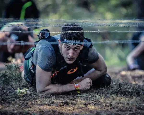 En man kryper under taggtråd under ett ocr sport-lopp.