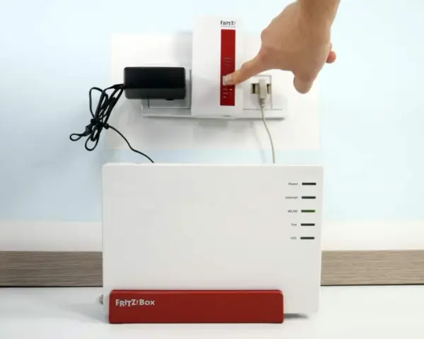 Finger drückt Knopf am Fritz!Repeater, um das **wifi repeater einrichten** zu starten. Fritz!Box steht daneben.