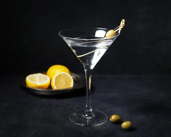 En klassisk vodka martini med en oliv på en tandpetare. Citroner ligger på en tallrik i bakgrunden.