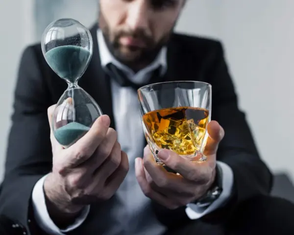 Mann im Anzug hält Sanduhr und Whiskyglas. Die Frage, ob kann Whisky schlecht werden, wird durch die vergehende Zeit und den edlen Tropfen symbolisiert.