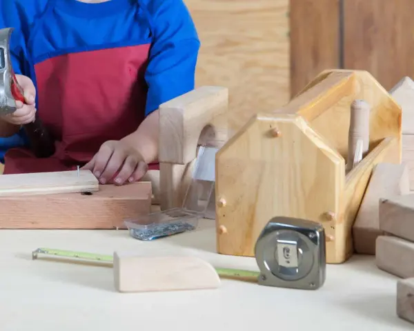Enfant bricolant avec un marteau, des clous, un mètre ruban et des outils en bois.