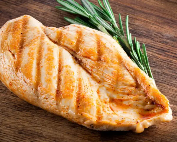 Grillowana pierś z kurczaka z rozmarynem na drewnianej desce. Zastanawiasz się, ile białka ma pierś z kurczaka? To świetne źródło!