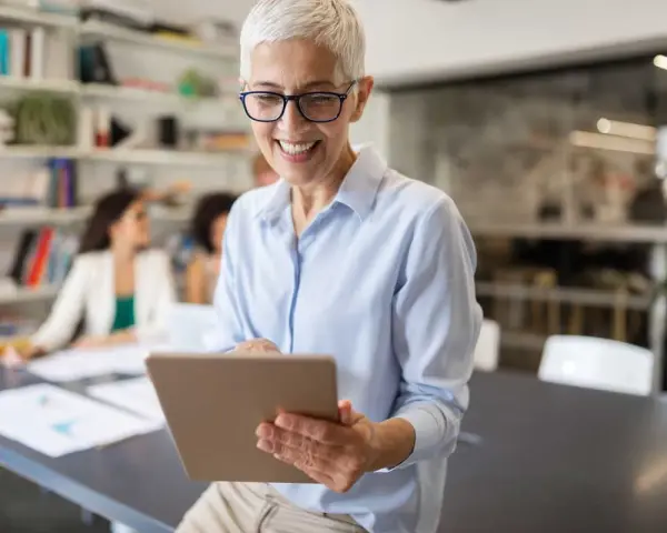 A smiling woman reviews a board chair job description on a tablet in a modern office.