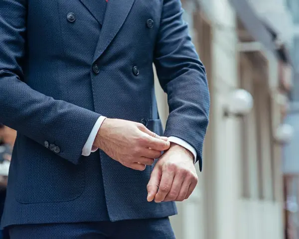 Uomo che sistema il polsino della sua giacca blu, un perfetto abbinamento giacca blu uomo per un look elegante.