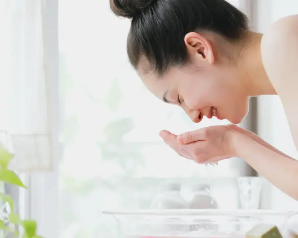 Eine Frau wäscht ihr Gesicht mit Seife und Wasser. Sie hält ihre Hände schöpfend unter fließendes Wasser, um ihr Gesicht zu reinigen.